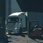 Flat style illustration of a truck being loaded at a warehouse dock in dramatic lighting, with a forklift and safety signage visible—ideal for encouraging viewers to Contact Our Compliance Team for logistics compliance help.